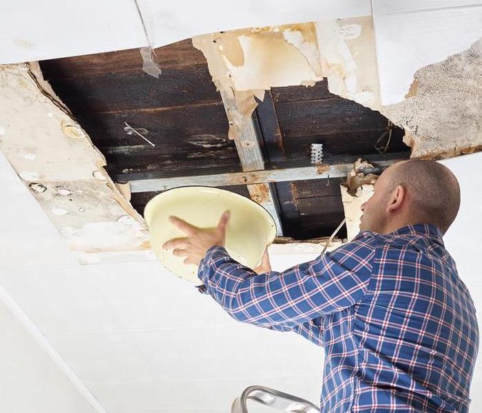 A man catching water dripping from a moldy ceiling